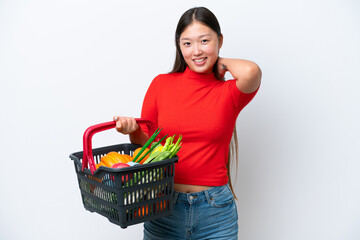 Obraz na płótnie Canvas Young Asian woman holding a shopping basket full of food isolated on white background laughing