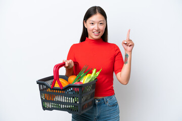 Fototapeta na wymiar Young Asian woman holding a shopping basket full of food isolated on white background pointing up a great idea