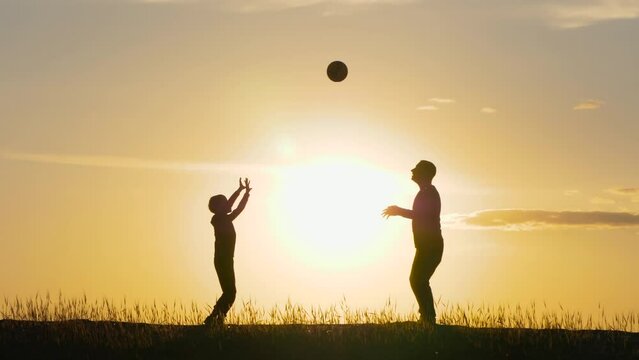 Black silhouette. The family plays volleyball at sunset. Dad and son play ball in nature. Happy family, active sports