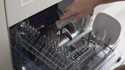 A woman puts a dirty frying pan in a small dishwasher