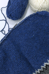 Blue wool yarn knitting on a metal needle with yarn balls on a white background, stockinette stitch knitted texture in progress