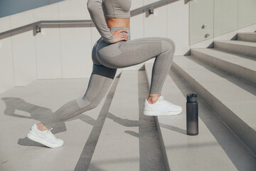 Slender woman in gray sportswear doing exercises outdoors on stair, forward lunges