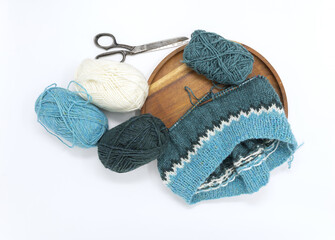 Turquoise white wool yarn knitting on a wooden needle with yarn balls, stockinette stitch knitted texture in progress