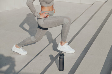 Slender woman in gray sportswear doing exercises outdoors on stair, forward lunges