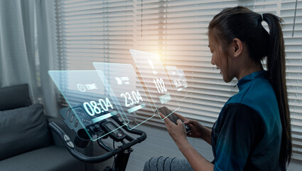 Cycling at home using a stationary exercise bike, Asian women using mobile phone tracking display heart rate for a healthy lifestyle technology, workout daily routine, racing sport activity training.