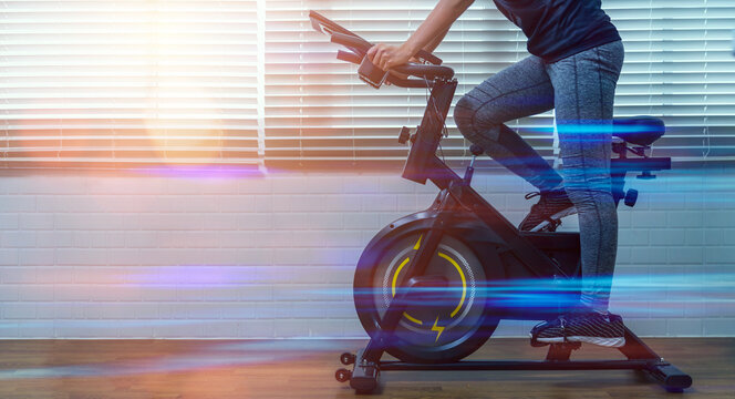 Cycling at home using a stationary exercise bike, Asian women using mobile phone tracking display heart rate for a healthy lifestyle technology, workout daily routine, racing sport activity training. - Powered by Adobe