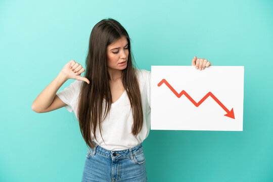 Young caucasian woman isolated on blue background holding a sign with a decreasing statistics arrow symbol and doing bad signal