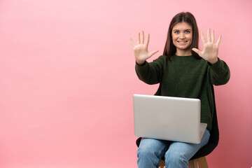 Young caucasian woman sitting on a chair with her laptop isolated on pink background counting ten with fingers