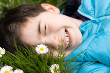 Obraz na płótnie Canvas boy kid child collecting flowers daisy white or dandelions on field.adorable preschooler with daisy through lips. spring amazing wallpaper.kid falling down next to puddle.lying on ground in park