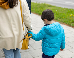 mother and son walking on sidewalk in city woman holding child boy hand.mommy explain is prohibited...