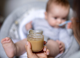 cute adorable boy child eating food from jar mashed puree.mother woman hand feeding infant...