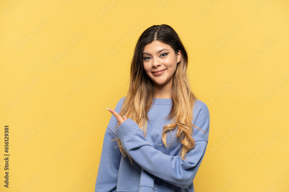 Wall mural Young Russian girl isolated on yellow background pointing to the side to present a product