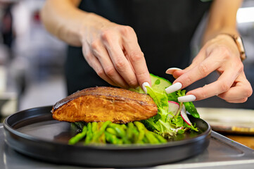 woman chef hand cooking salmon steak with asparagus and salad