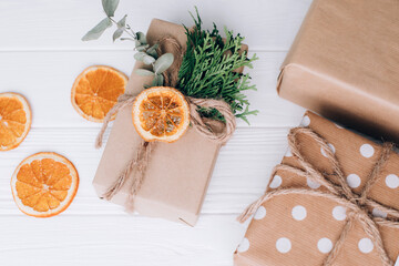 The gift is wrapped in brown paper and tied with twine with thuja and eucalyptus on a white wooden...