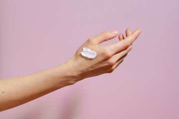 Fragile female hand with white cream smear on purple isolated background. Concept of cosmetics for...