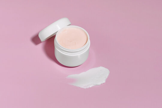 Top view of open round jar of face cream and white smear or swotch on purple isolated background. Concept of skin care products, cosmetic products for daily care