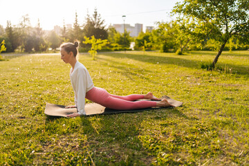 Side view of beautiful fit young woman in sportswear working out outdoors at summer park, doing stretching exercises standing in pose dog muzzle up, sun salutation complex. Upward-Facing Dog Breakdown