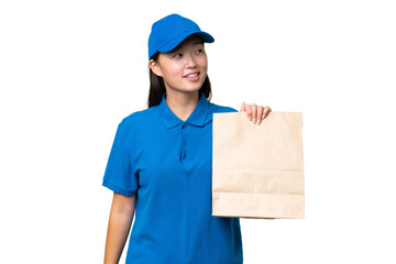 Young Asian woman taking a bag of takeaway food over isolated background looking to the side and smiling