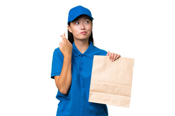 Young Asian woman taking a bag of takeaway food over isolated background with fingers crossing and wishing the best