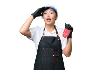 Young caucasian woman wearing an apron and serving fresh cut meat over isolated background doing surprise gesture while looking to the side