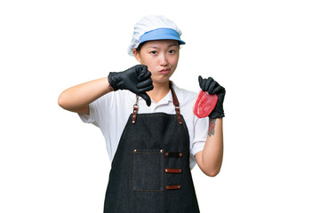 Young caucasian woman wearing an apron and serving fresh cut meat over isolated background showing thumb down with negative expression