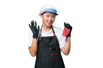 Young caucasian woman wearing an apron and serving fresh cut meat over isolated background saluting with hand with happy expression