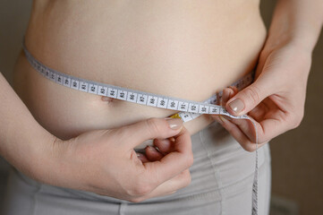 A fat obese woman measures her waist with a centimeter tape, close-up. Weight loss, obesity. Woman after childbirth.