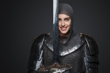 Beautiful woman is dressed in Knightly armor, is smiling wide, and confidently posing with a sword...