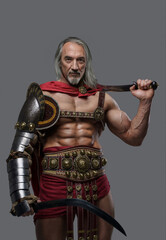 Fototapeta na wymiar Distinguished elder gladiator exudes power and strength in elegant, lightweight armor, wielding two gladius swords with confidence against a grey background