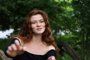 Portrait of smiling ginger girl with long red hair and freckles pulling her hands to the camera. Young sensual model, natural female beauty