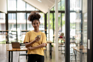 Smiling African American businesswoman, Freelance business woman in casual look standing in coworks space and cafe, using mobile phone.