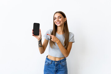 Smiling woman pointing on smartphone standing on white background.