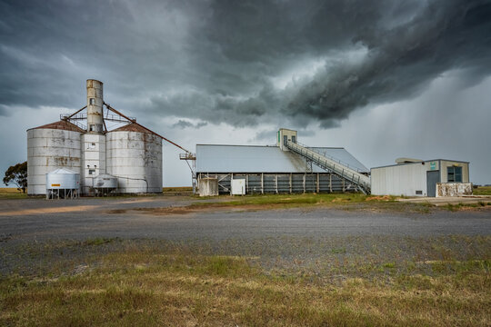 Rain falling from a dramatic grey stormfront over grain storage silos in a rural setting