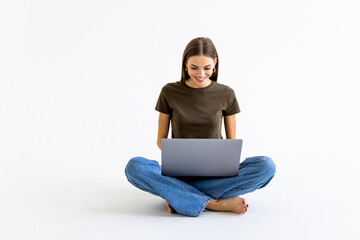 Young woman sitting on the floor and using laptop on white background