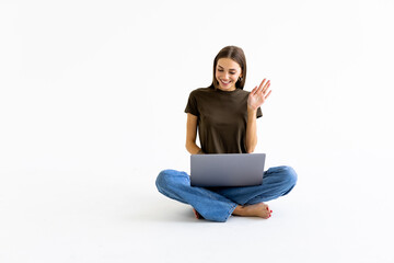 Young woman sitting on floor with laptop make video call on white background