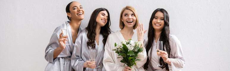 bridal party, multicultural women holding glasses with champagne, bride with white flowers showing her engagement ring, bridesmaids, diversity, positivity, bridal bouquet, grey background, banner