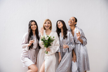 bridal party, multicultural women holding glasses with champagne, bride with white flowers showing...