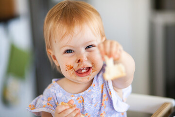 One year old baby with messy face holding out piece of toast to share
