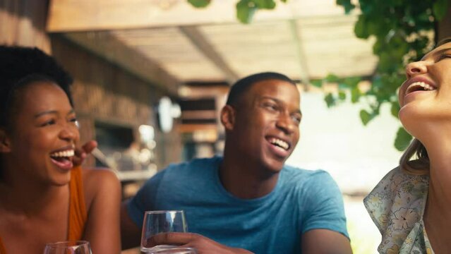 Close up of smiling group of multi-cultural friends outdoors on holiday or at home drinking wine together  - shot in slow motion