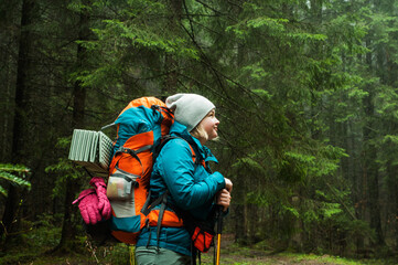 a girl with a big tourist backpack in a green coniferous forest, the beauty of nature, the landscape in the Carpathian mountains, travel, hiking, walks in the park, retreat, vacation, adventure