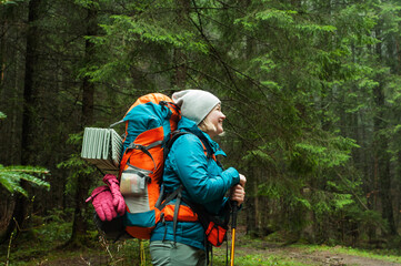 a girl with a big tourist backpack in a green coniferous forest, the beauty of nature, the landscape in the Carpathian mountains, travel, hiking, walks in the park, retreat, vacation, adventure