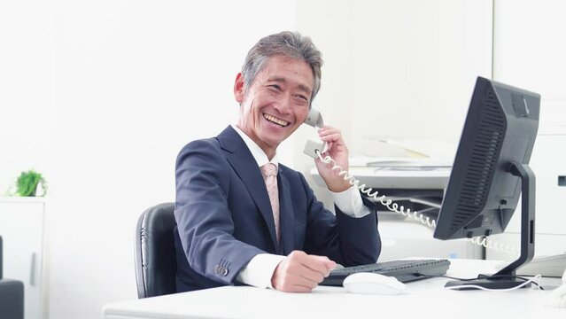 オフィスで電話をする管理職の男性