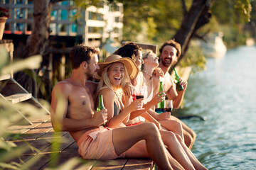 Happy group of people drinking on a dock by the water during the summer sunny day