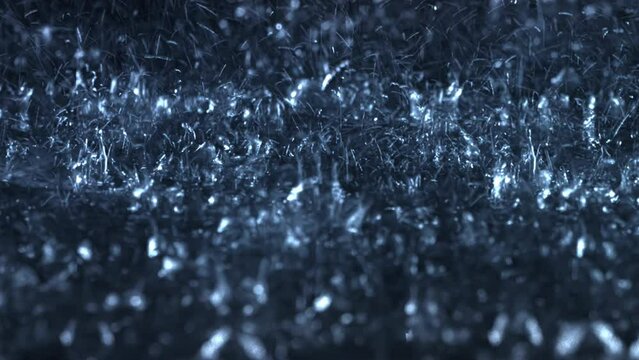 Heavy rain falls in front of the camera against black screen. Raindrops are splashing. Rain closeup VFX insert. Practical, seamlessly loopable footage. Heavy rainstorm hitting black surface.	