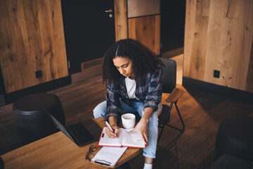 Fototapeta na wymiar Focused black woman taking notes in planner in cafe