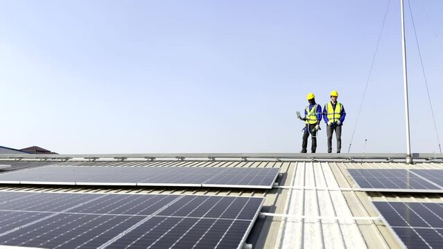 Modern solar farm on a roof under the sky. Workers in uniform and protective helmets discuss the solar panels installation.