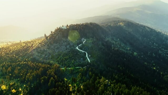 A path leads from Bavarian Forest to little house on top of mountain. Drone flies to cottage under sunset.
