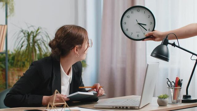 Young business woman working on office laptop with anxiety checking time on clock running late to work being in delay deadline. Manager freelancer girl looking at hour minutes worrying to be punctual