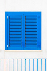 Minimalistic image of bright blue shutters on a white stone wall.