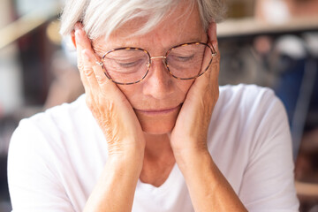 Close up portrait of unhappy senior woman touching her face with hands thinking to problems to solve. Bad migraine and health problems.